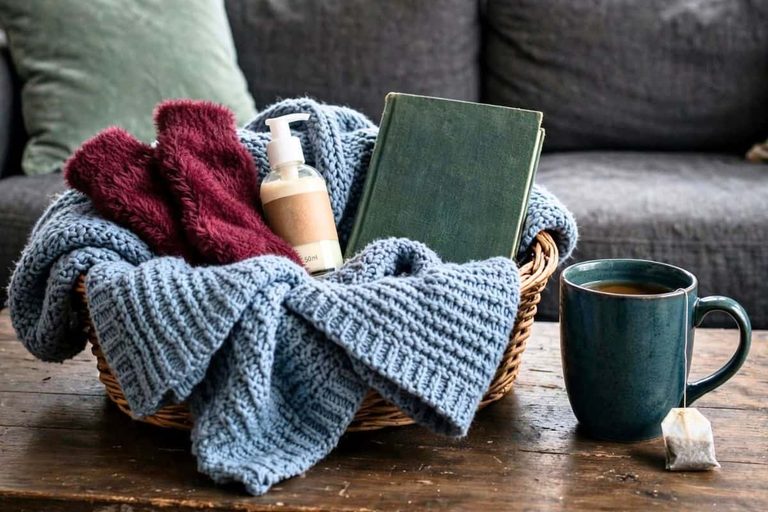 Winter self-care kit with a cozy blanket, warm socks, journal, lotion, and mug of tea.