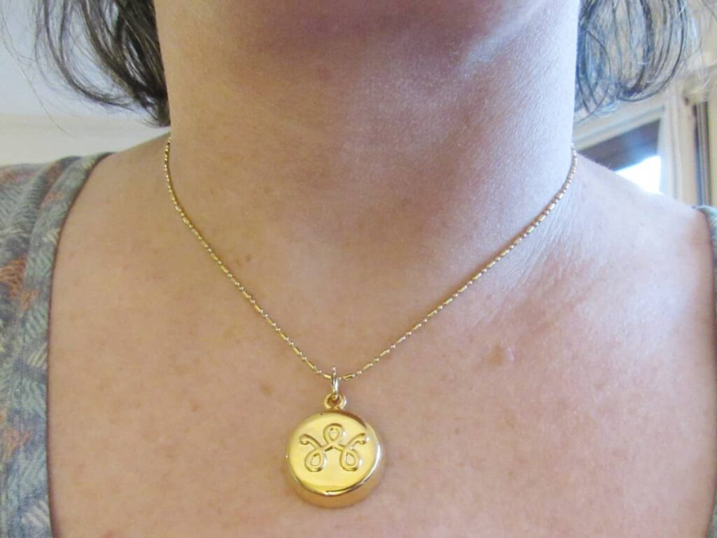 Close-up of a gold necklace with a round pendant worn around a woman’s neck, resting against the chest.