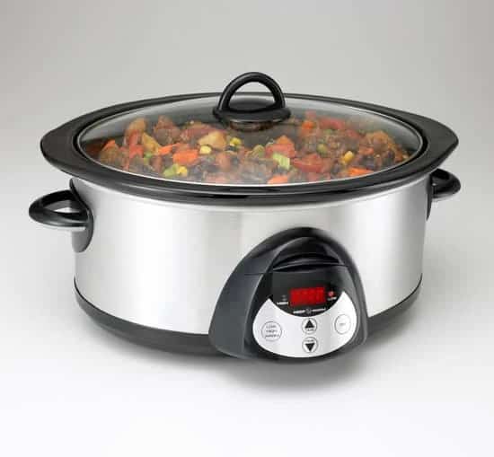 Stainless steel slow cooker with glass lid, filled with a hearty stew of meat and vegetables, featuring a digital control panel on the front.