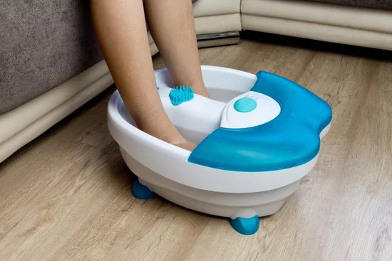 Feet soaking in an electric foot spa massager with water, featuring a blue and white design on a wooden floor.