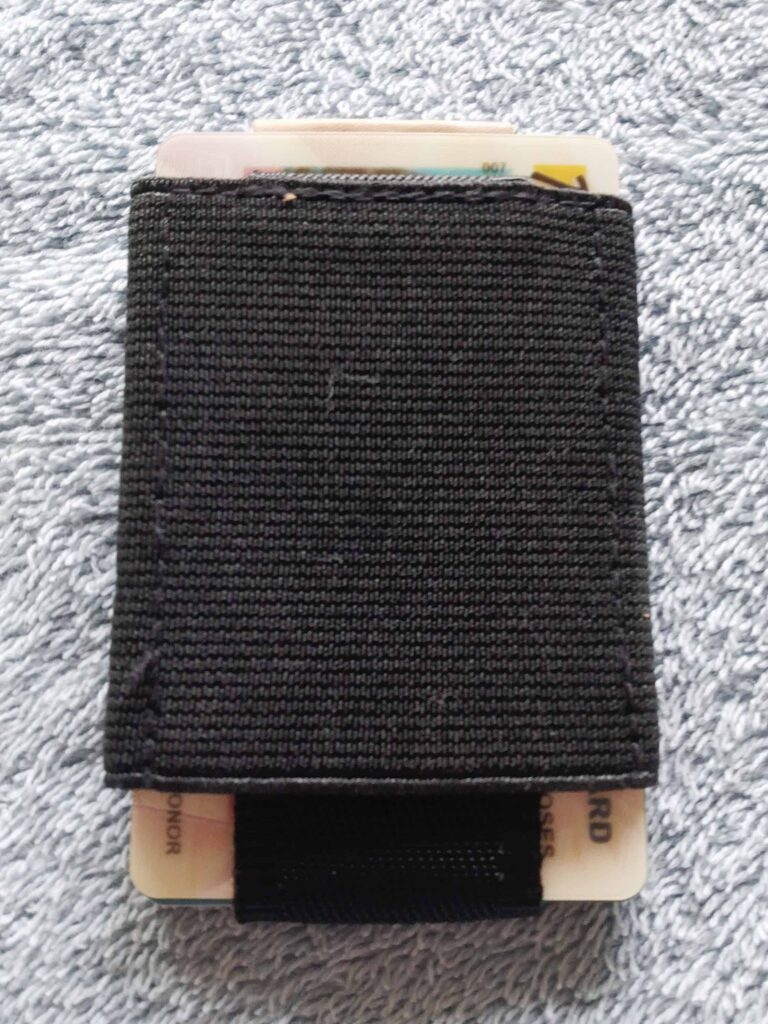 Slim black minimalist wallet with cards partially visible, resting on a textured surface.
