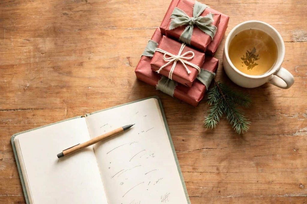 Open notebook, pen, tea, and wrapped gifts on a wooden table.
