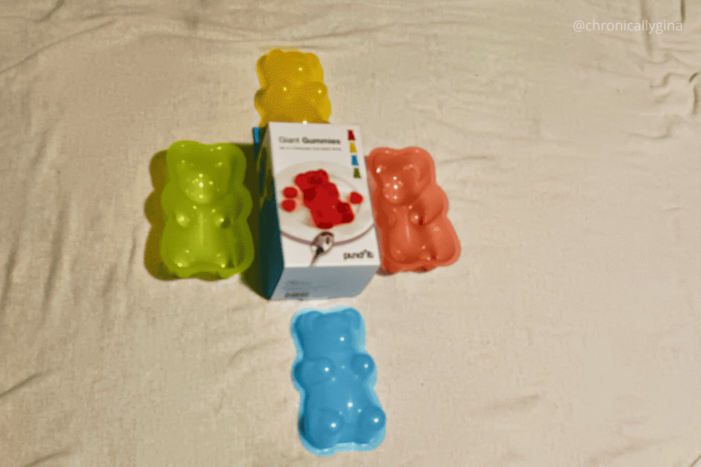 Colorful gummy bear–shaped silicone molds in yellow, green, red, and blue arranged around a box of Giant Gummies candy molds—an adorable and creative budget-friendly gift idea for candy lovers or DIY enthusiasts.