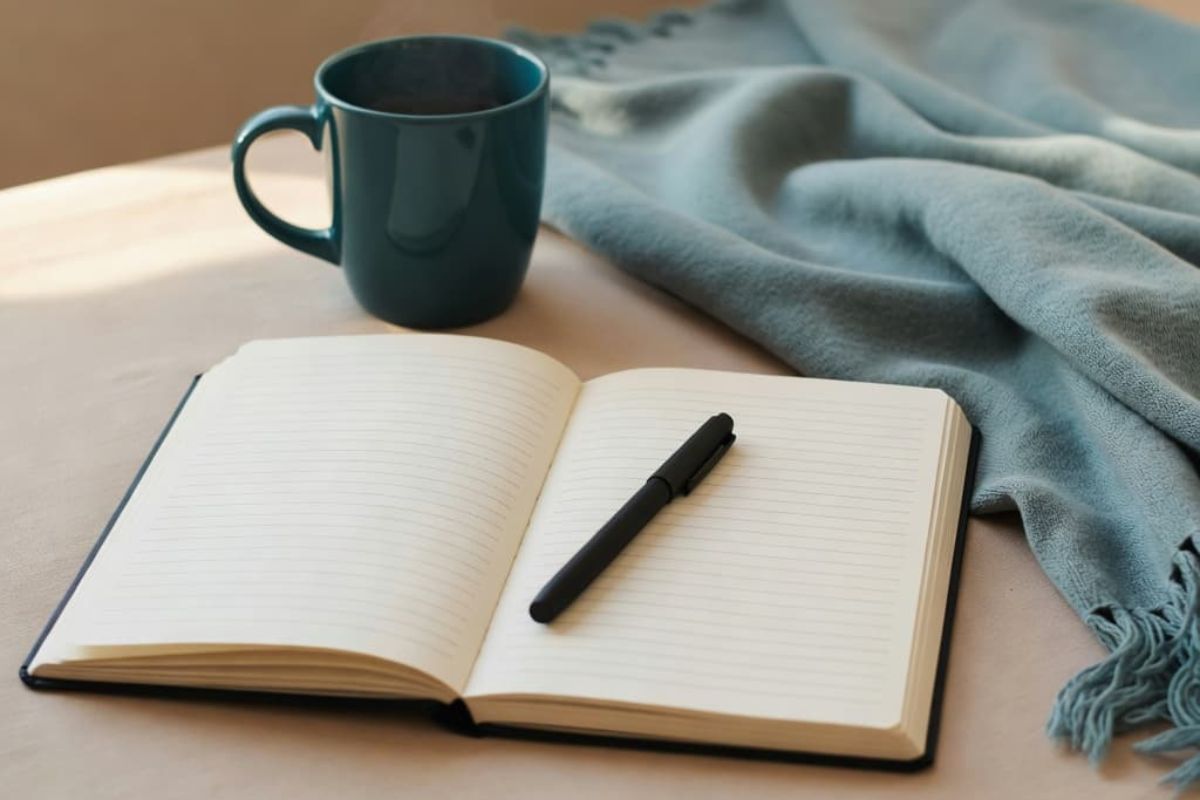 Open journal with pen, teal mug, and soft blanket for journaling prompts for anxiety.